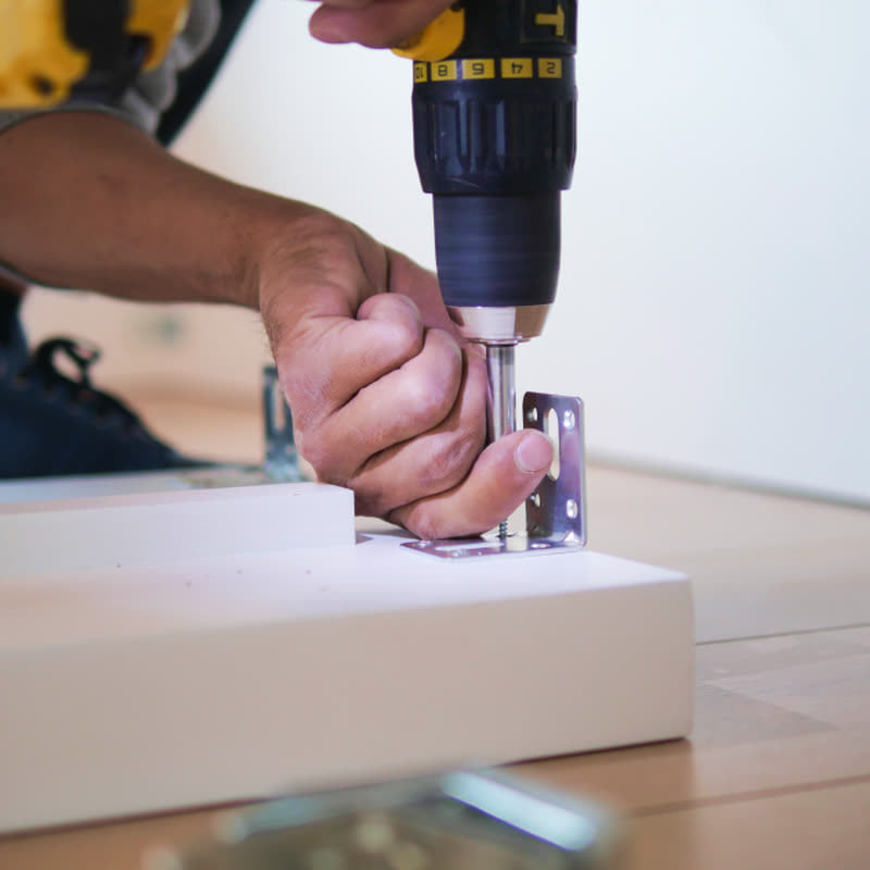 Installer fixing a hinge to a cabinet door with a cordless drill