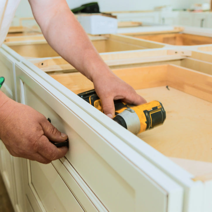 Installer fitting a cabinet drawer with a power drill